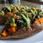 Close-up of two Loaded Veggie Stuffed Sweet Potatoes topped with quinoa, black beans, corn, and a bright green sauce.
