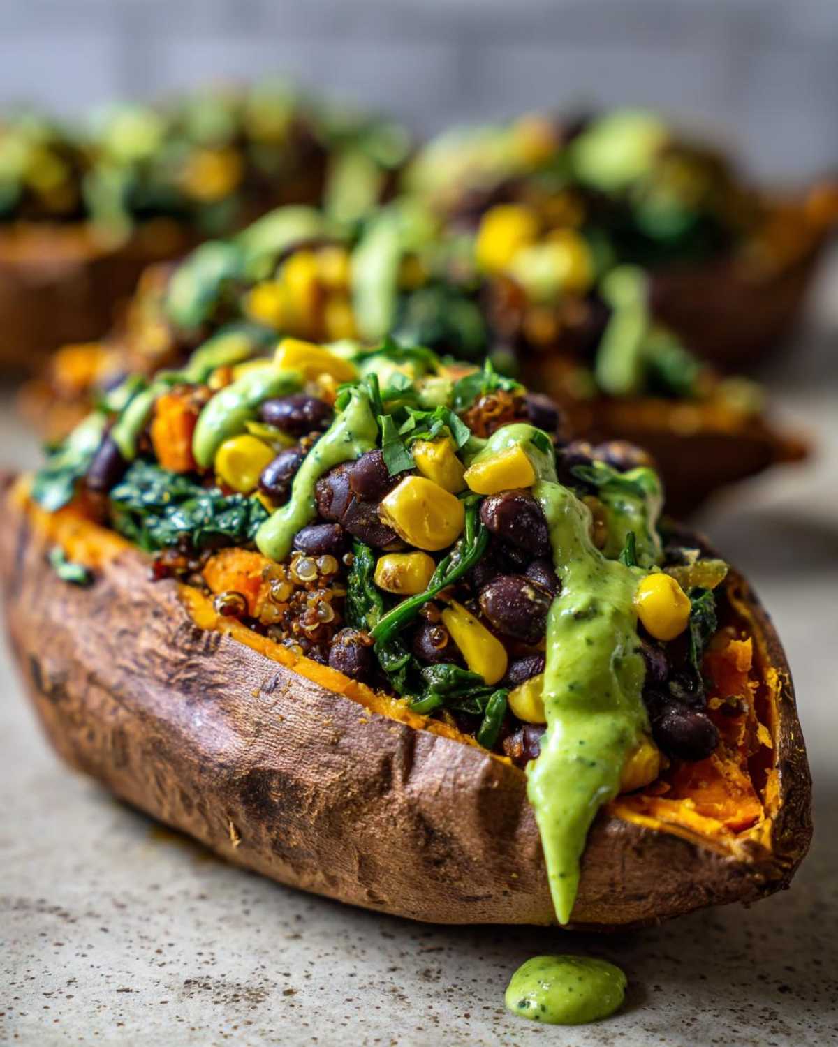 Close-up of a Loaded Veggie Stuffed Sweet Potato topped with black beans, corn, spinach, and a creamy green sauce.