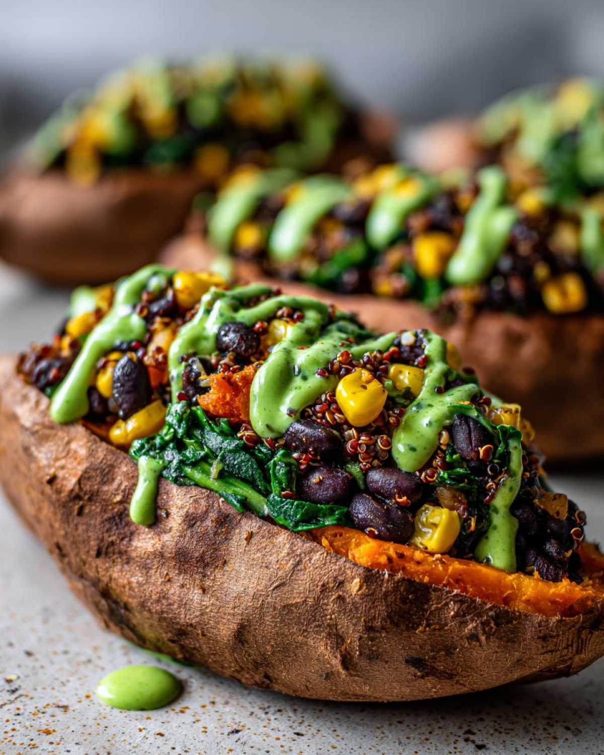 Close-up of Loaded Veggie Stuffed Sweet Potatoes topped with black beans, corn, quinoa, spinach, and a bright green drizzle.