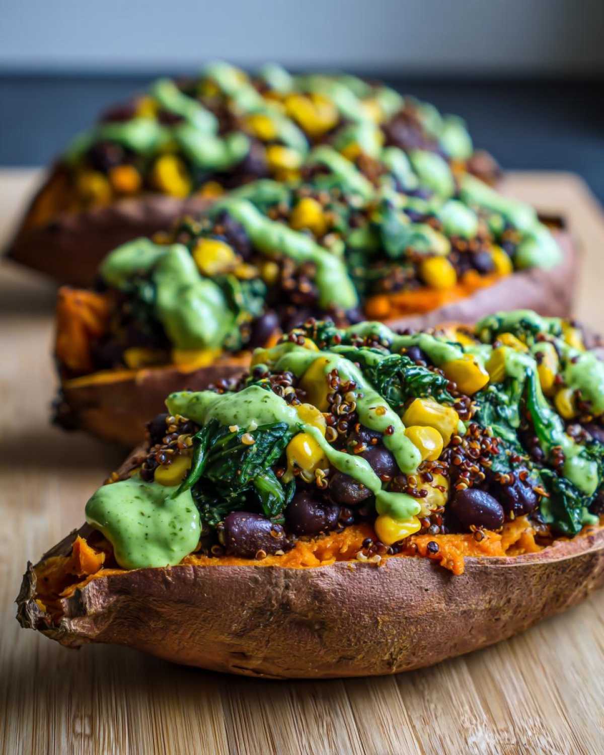 Three Loaded Veggie Stuffed Sweet Potatoes topped with black beans, corn, quinoa, spinach, and a creamy green sauce.