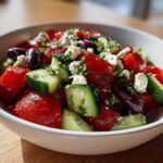 Close-up of vibrant Mediterranean Cucumber Tomato Salad with feta cheese, olives, and herbs in a white bowl.
