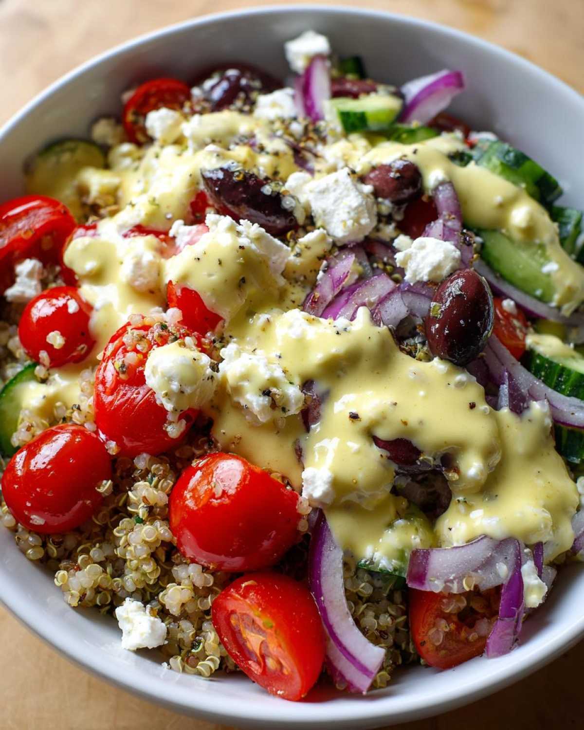 Close-up of a vibrant Mediterranean Quinoa Bowl topped with cherry tomatoes, feta, olives, and lemon tahini sauce.