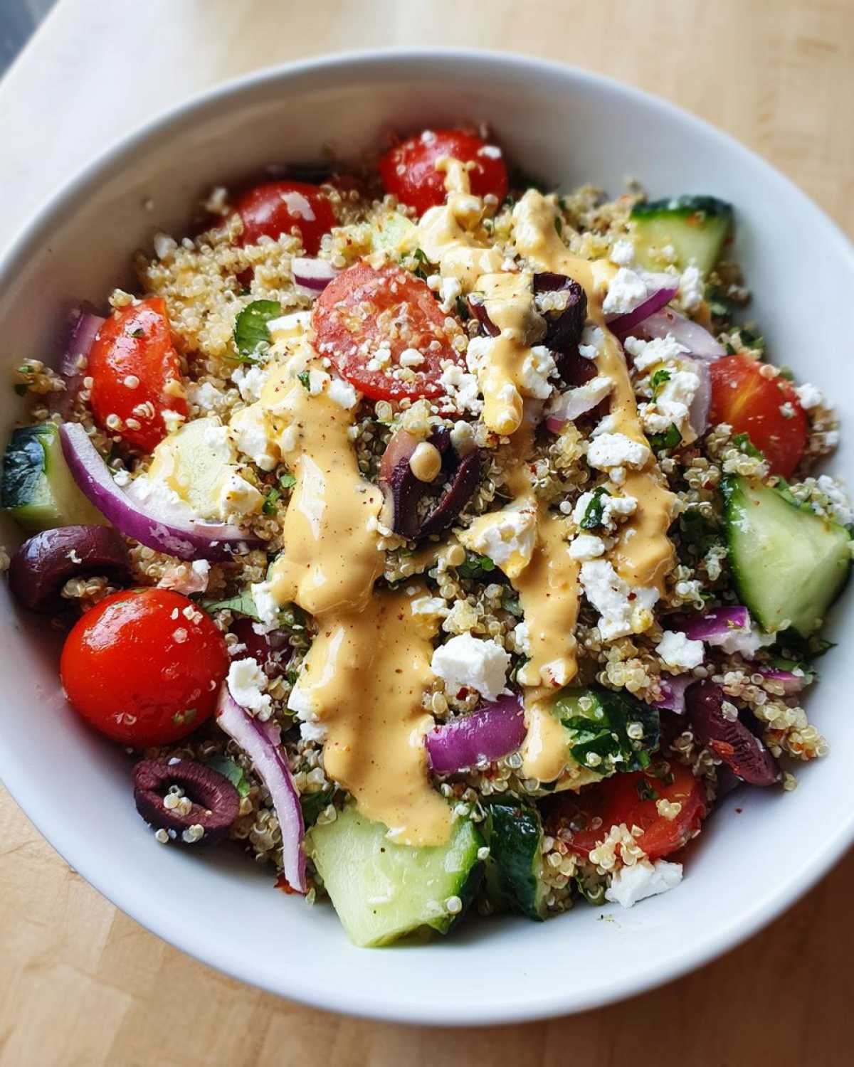 Close-up of a Mediterranean Quinoa Bowl topped with feta, olives, tomatoes, and drizzled with Lemon Tahini Sauce.