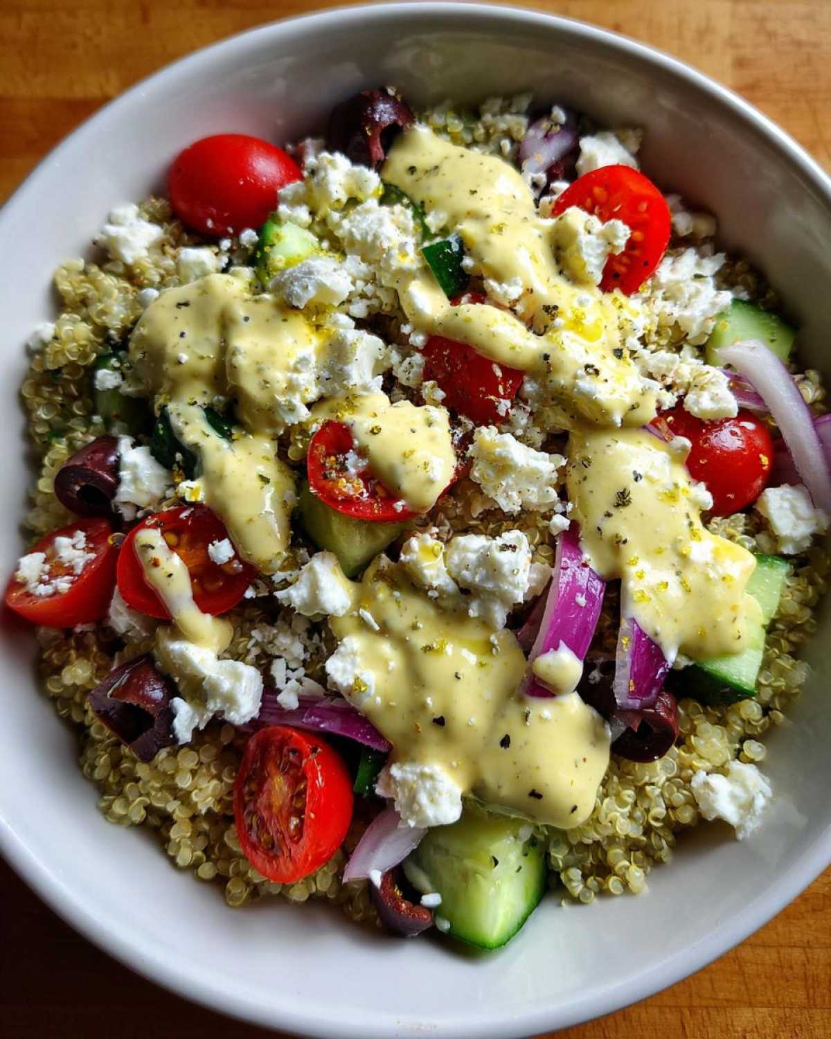 Close-up of a Mediterranean Quinoa Bowl topped with feta, tomatoes, cucumber, and drizzled with lemon tahini sauce.