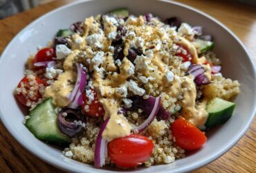 Close-up of a vibrant Mediterranean Quinoa Bowl topped with feta, olives, tomatoes, cucumber, and lemon tahini sauce.