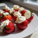 A plate of bright red No-Bake Cheesecake Stuffed Strawberries topped with swirls of white cream.