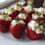 A plate of fresh, bright red No-Bake Cheesecake Stuffed Strawberries topped with creamy white filling.
