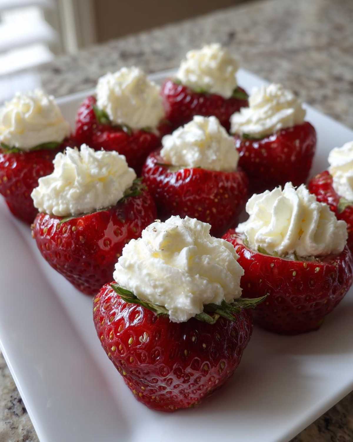 A platter of bright red No-Bake Cheesecake Stuffed Strawberries topped with whipped cream.