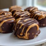 Close-up of several No-Bake Chocolate Covered Banana Bites drizzled with peanut butter on a white plate.