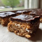 A close-up of a layered No-Bake Chocolate Peanut Butter Oat Bars showing the oat base, peanut butter layer, and chocolate topping.