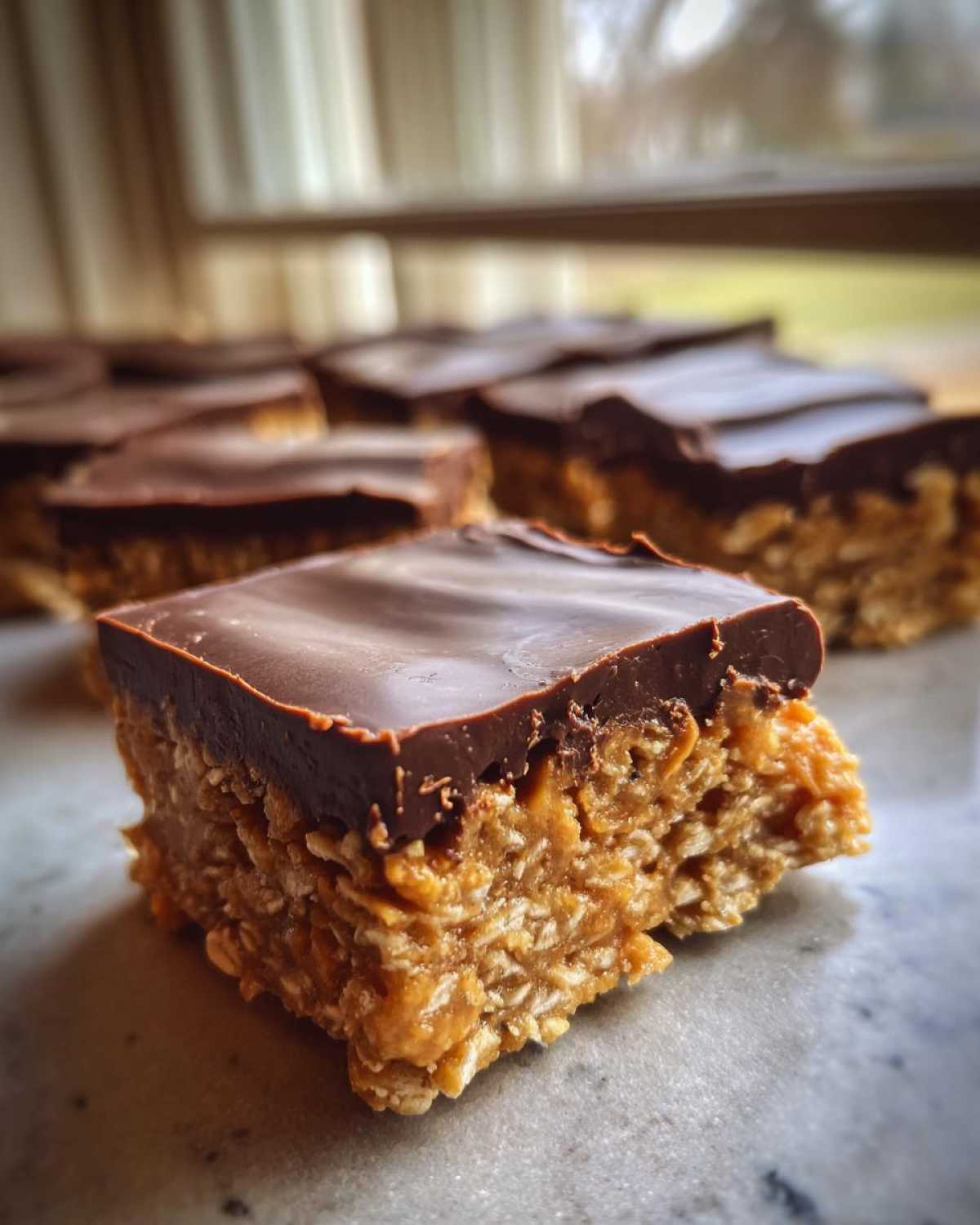 A close-up of a square No-Bake Chocolate Peanut Butter Oat Bars with a thick chocolate topping.
