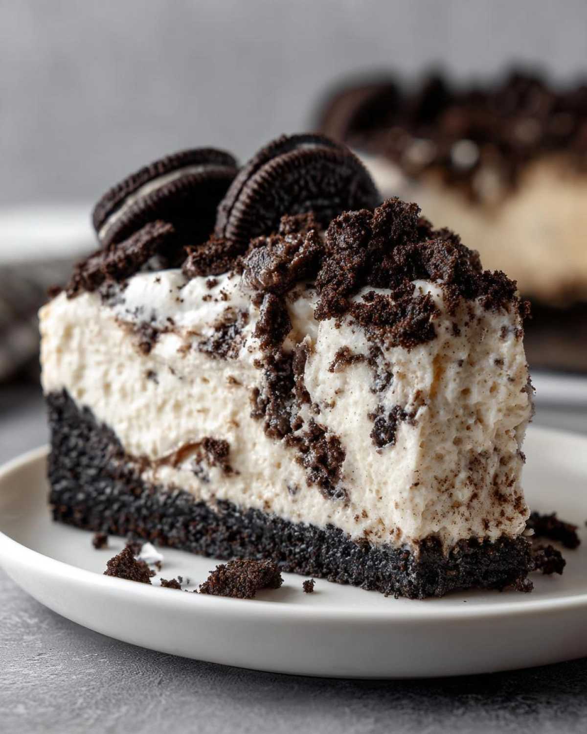 A close-up of a creamy slice of No-Bake Oreo Cheesecake with a thick Oreo crust and cookie crumbles on top.