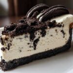 A perfect slice of No-Bake Oreo Cheesecake showing a thick Oreo crust, creamy filling, and chocolate cookie crumble topping.