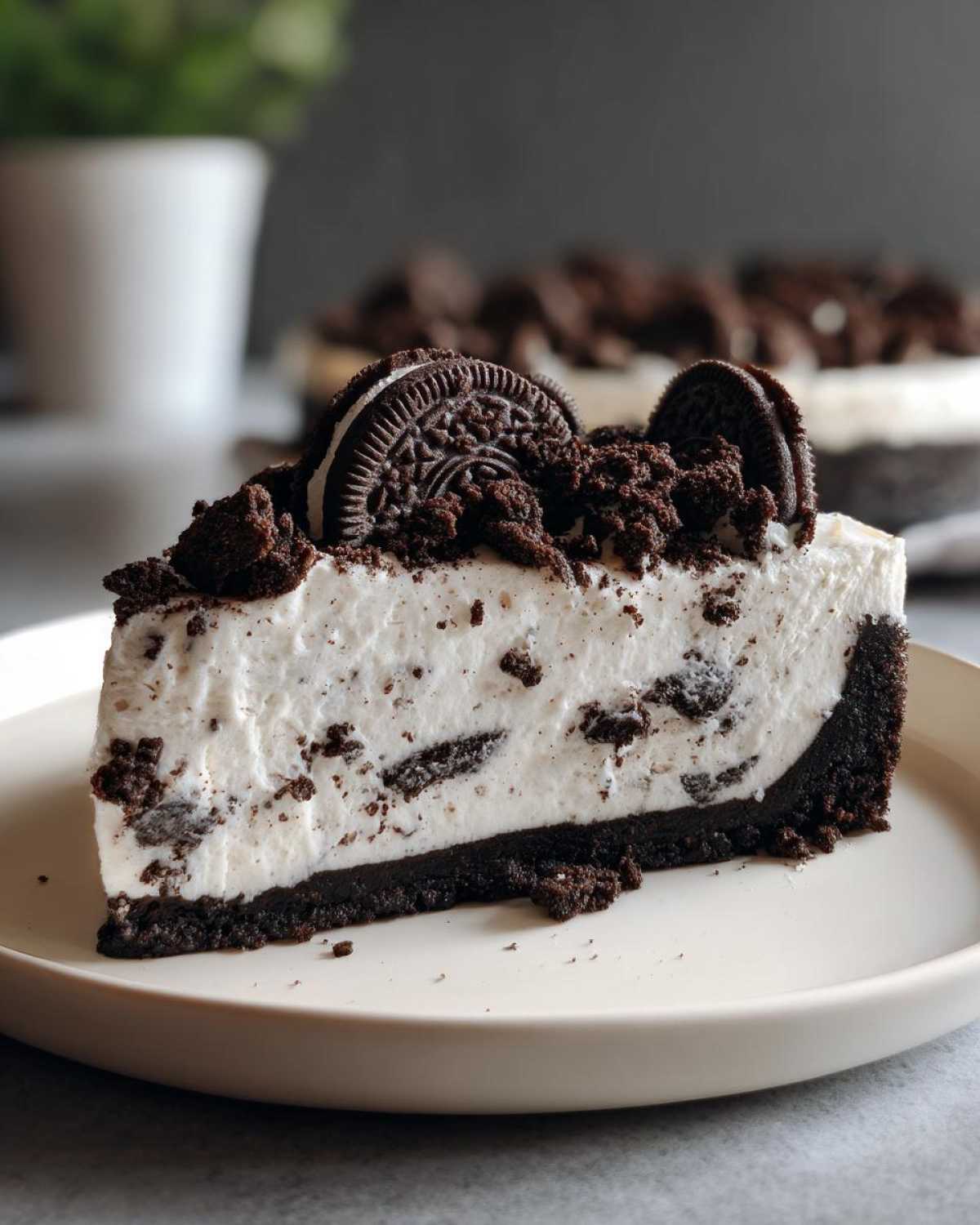 A perfect slice of No-Bake Oreo Cheesecake with a thick Oreo crust and creamy filling, topped with crumbs and whole Oreos.