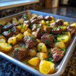 Close-up of One-Pan Garlic Butter Steak Bites and Potatoes glistening in butter sauce on a sheet pan.