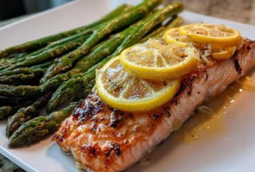 Close-up of a perfectly cooked One-Pan Lemon Garlic Salmon with asparagus spears, topped with lemon slices.