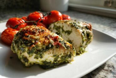 A close-up of sliced One-Pan Pesto Chicken with Tomatoes, topped with green pesto and served with roasted cherry tomatoes.