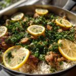A skillet filled with One-Pot Chicken and Rice with Lemon and Herbs, topped generously with fresh parsley and lemon slices.