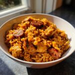 A white bowl filled with flavorful One-Pot Chicken Jambalaya, featuring rice, chicken chunks, and slices of andouille sausage.