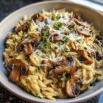A close-up of a bowl of One-Pot Creamy Mushroom Orzo topped with sautéed mushrooms and grated cheese.