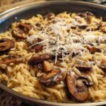 Close-up of One-Pot Creamy Mushroom Orzo topped with shaved Parmesan cheese in a skillet.