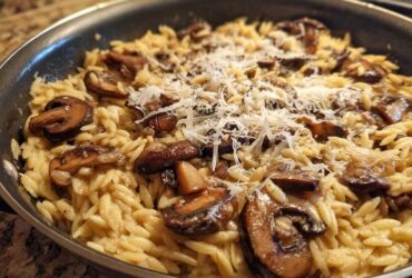 Close-up of One-Pot Creamy Mushroom Orzo topped with shaved Parmesan cheese in a skillet.