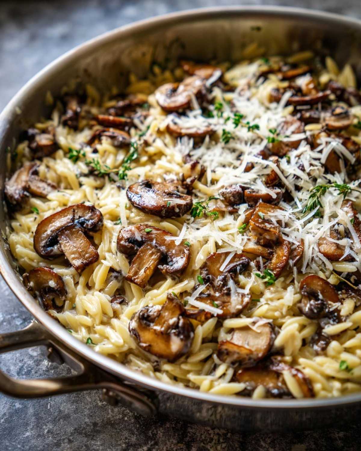 Close-up of One-Pot Creamy Mushroom Orzo topped with shaved Parmesan and fresh thyme.