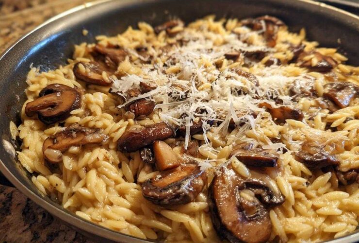 Close-up of One-Pot Creamy Mushroom Orzo topped with shaved Parmesan cheese in a skillet.