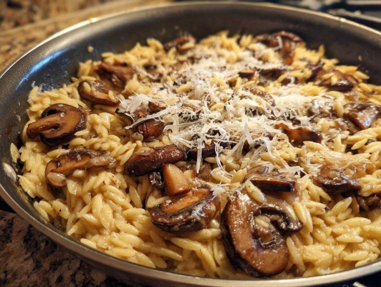 Close-up of One-Pot Creamy Mushroom Orzo topped with shaved Parmesan cheese in a skillet.