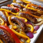 Close-up of browned sausages roasted with colorful bell peppers and onions on a sheet pan.