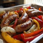 Close-up of browned sausages roasted with colorful bell peppers and onions on a sheet pan.