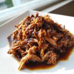 A close-up of saucy Slow Cooker Honey Garlic Pulled Pork piled high on a white plate.