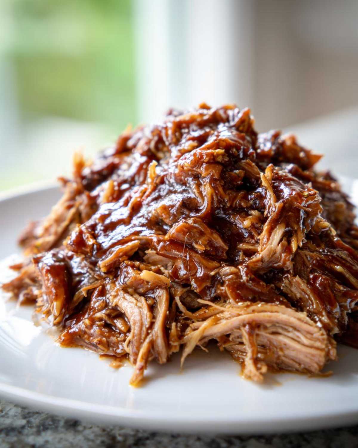 Close-up of tender, saucy Slow Cooker Honey Garlic Pulled Pork piled high on a white plate.
