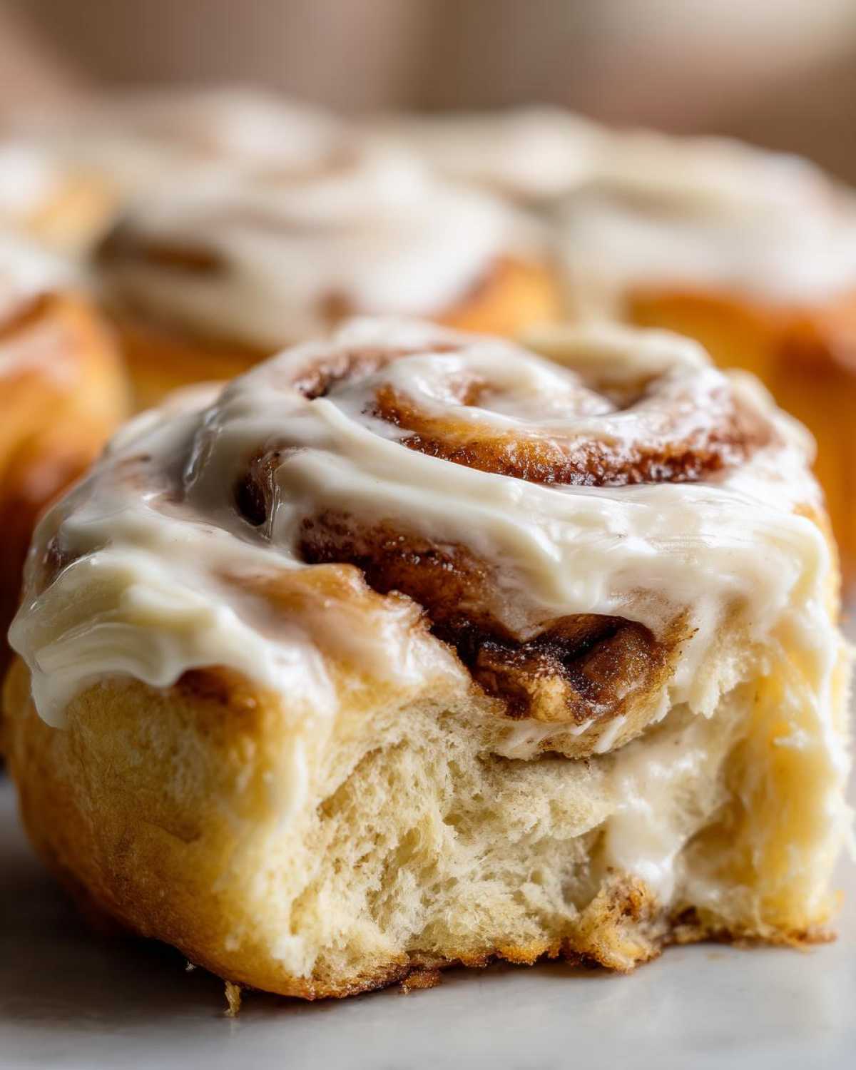 Close-up of a soft Gluten-Free Cinnamon Roll with a bite taken out, showing the fluffy interior and thick white frosting.