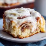 Close-up of a soft, fluffy Gluten-Free Cinnamon Roll topped generously with thick white cream cheese frosting.