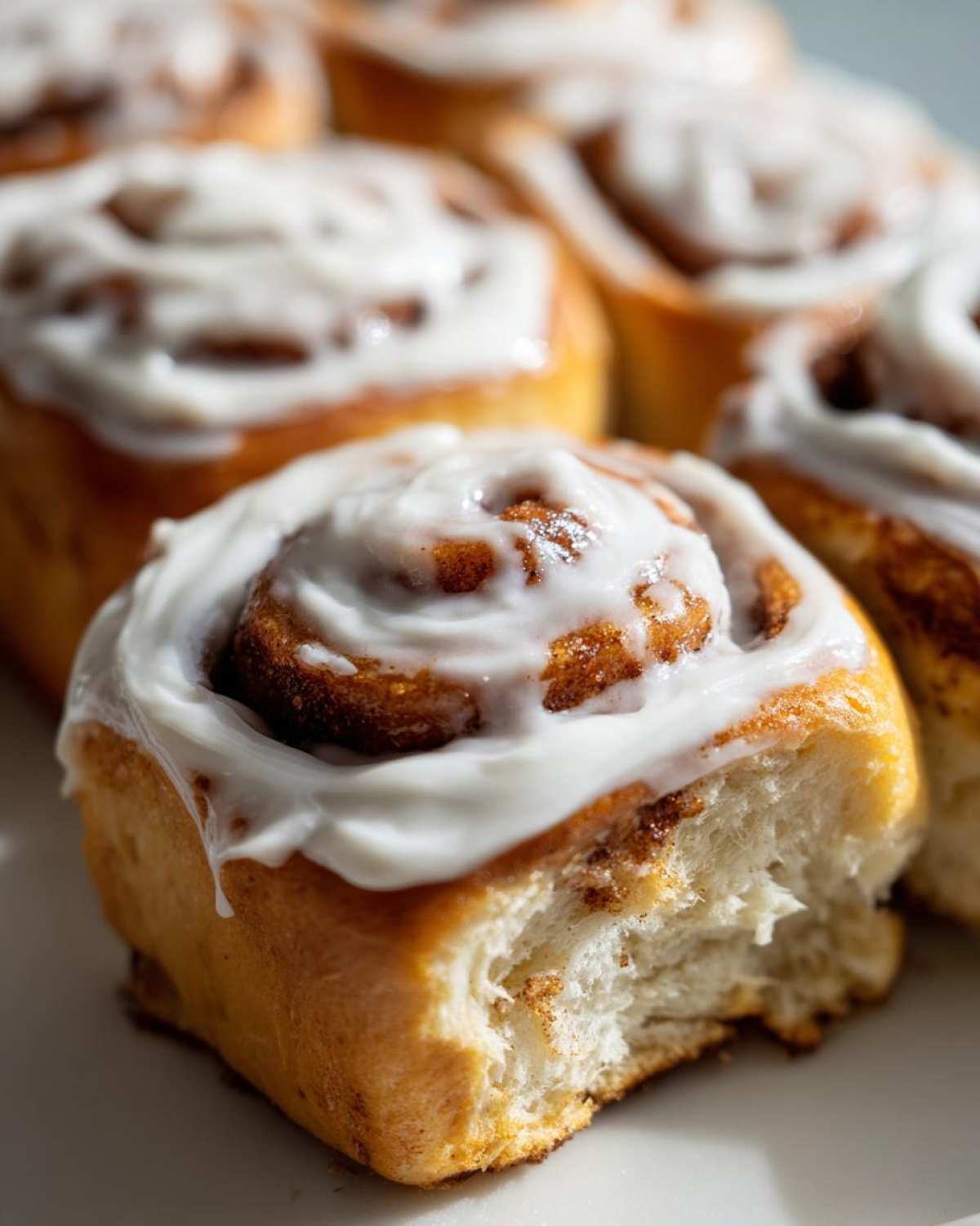 Close-up of a soft Gluten-Free Cinnamon Roll with a bite taken out, showing the fluffy interior and thick white frosting.