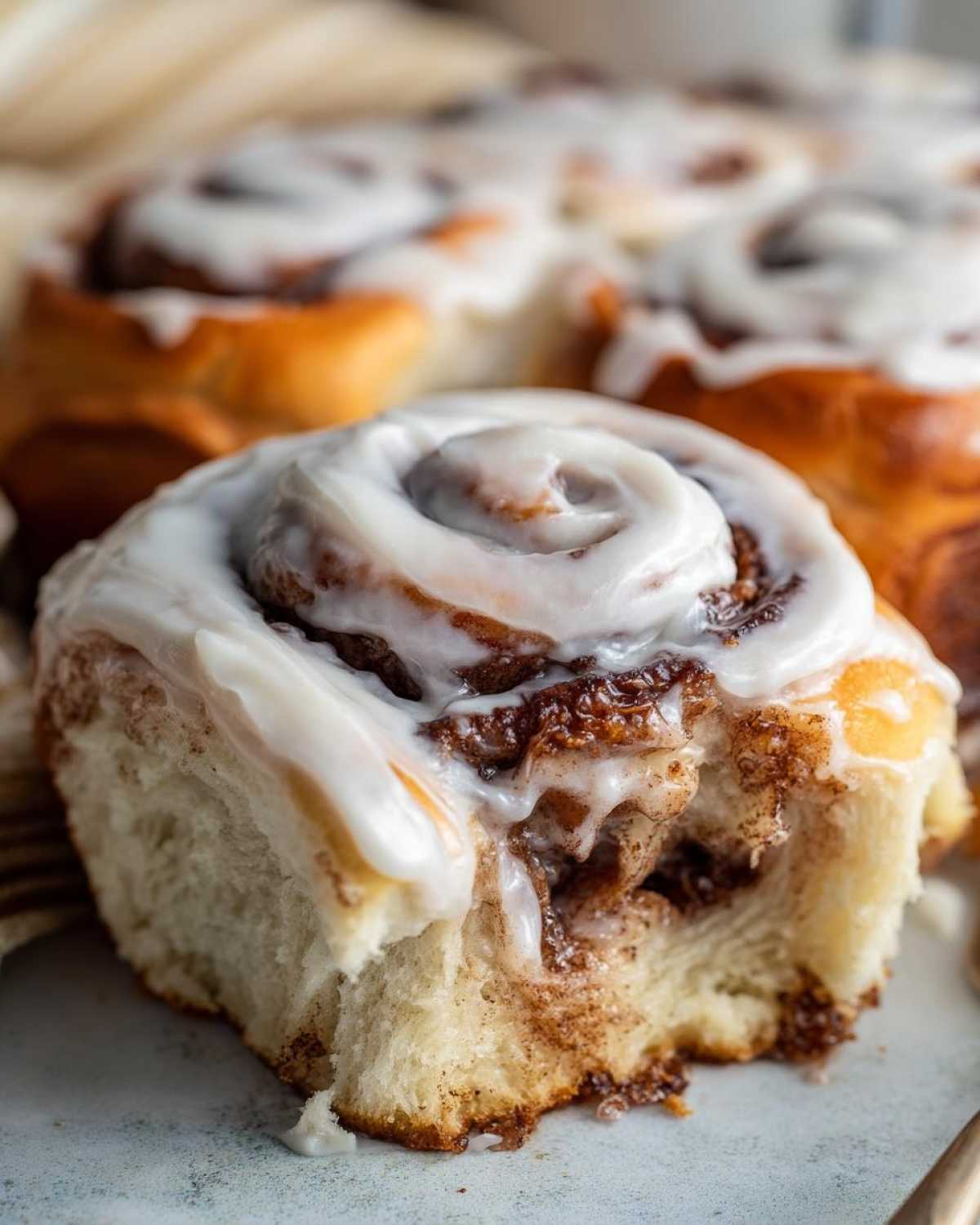 Close-up of a soft Gluten-Free Cinnamon Roll with gooey cinnamon filling and thick white frosting.
