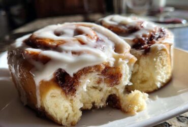 Close-up of two soft Gluten-Free Cinnamon Rolls drizzled with white icing on a white plate.