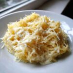 A close-up serving of Spaghetti Squash Alfredo tossed in a creamy white sauce and topped with grated cheese.
