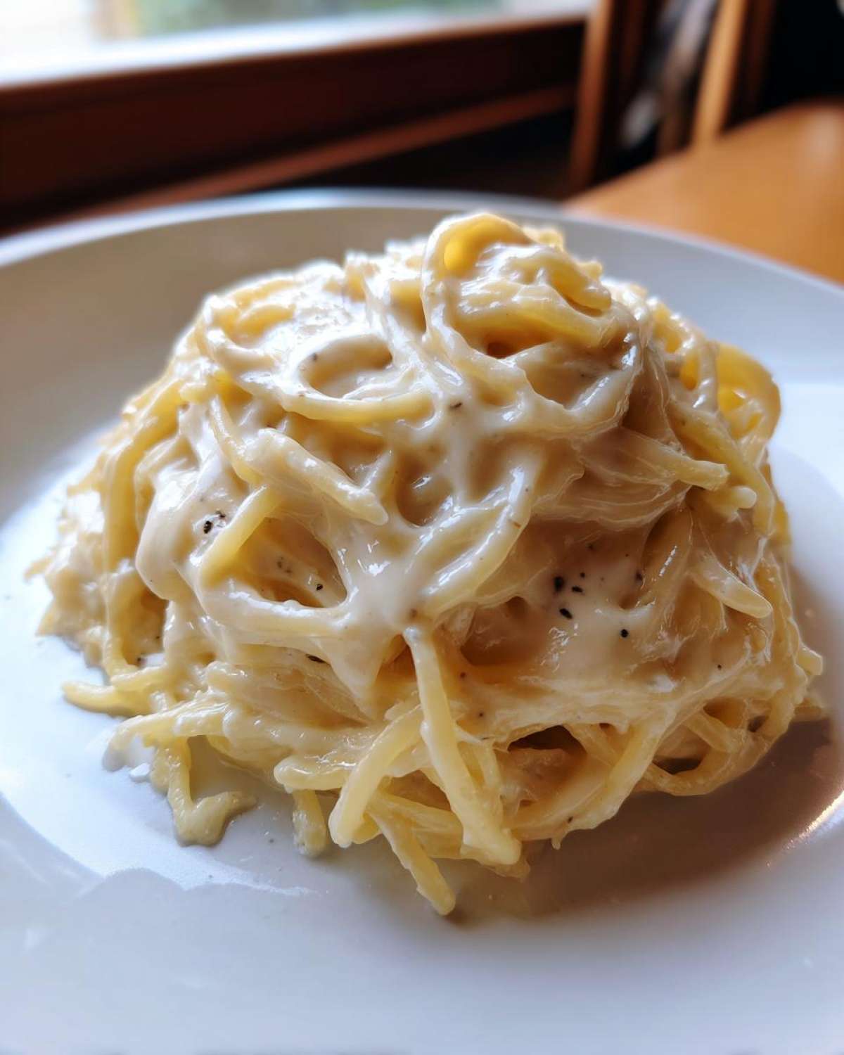 Close-up of a mound of creamy Spaghetti Squash Alfredo tossed in a rich white sauce on a white plate.