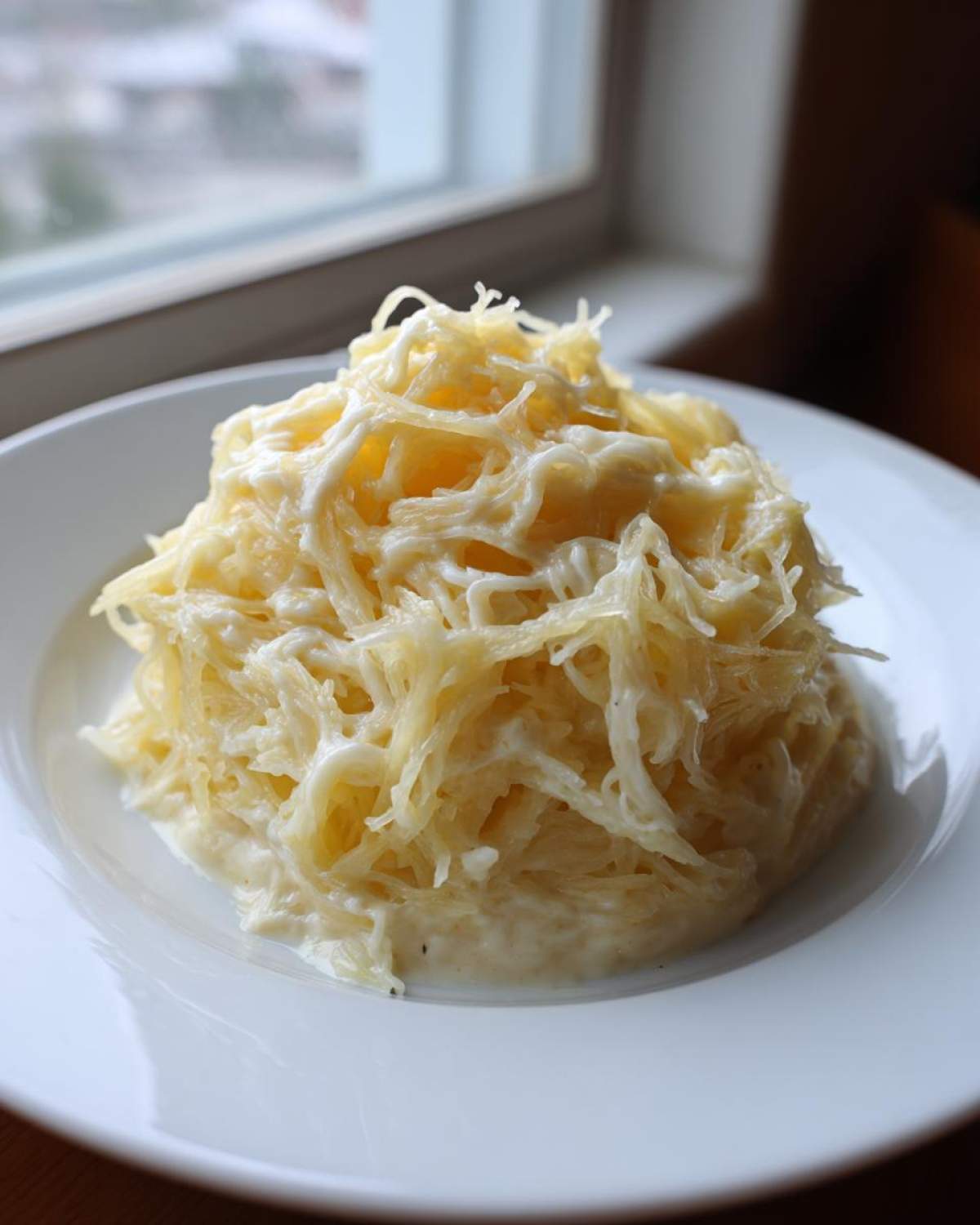 A mound of creamy Spaghetti Squash Alfredo served on a white plate near a window.