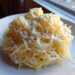 Close-up of a serving of Spaghetti Squash Alfredo, showing squash strands coated in white sauce and topped with black pepper.