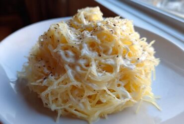 Close-up of a serving of Spaghetti Squash Alfredo, showing squash strands coated in white sauce and topped with black pepper.