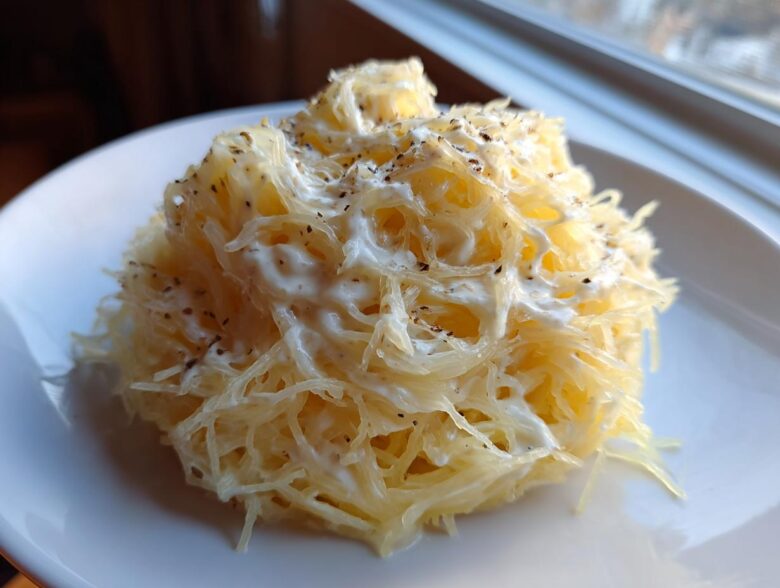 Close-up of a serving of Spaghetti Squash Alfredo, showing squash strands coated in white sauce and topped with black pepper.