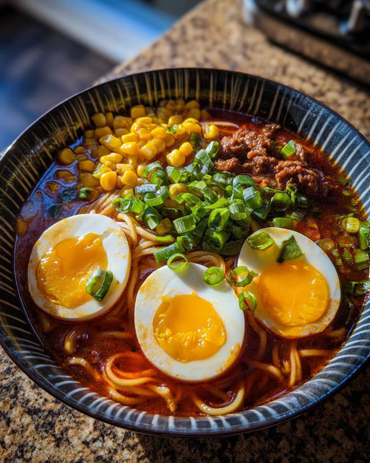A close-up of a bowl of Spicy Miso Ramen with soft-boiled eggs, corn, ground meat, and chopped green onions.