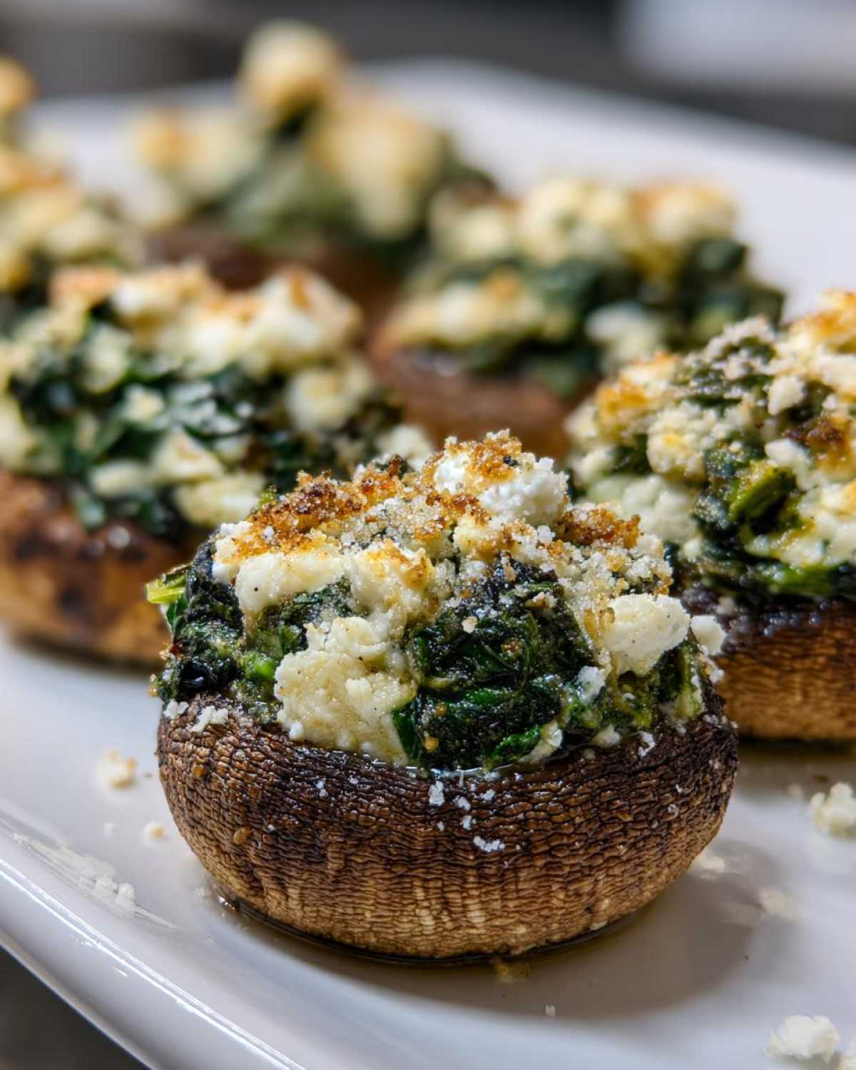 A close-up of baked Spinach and Feta Stuffed Mushrooms topped with breadcrumbs on a white platter.