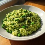 A close-up of creamy Spring Pea and Mint Risotto topped with whole bright green peas in a white bowl.