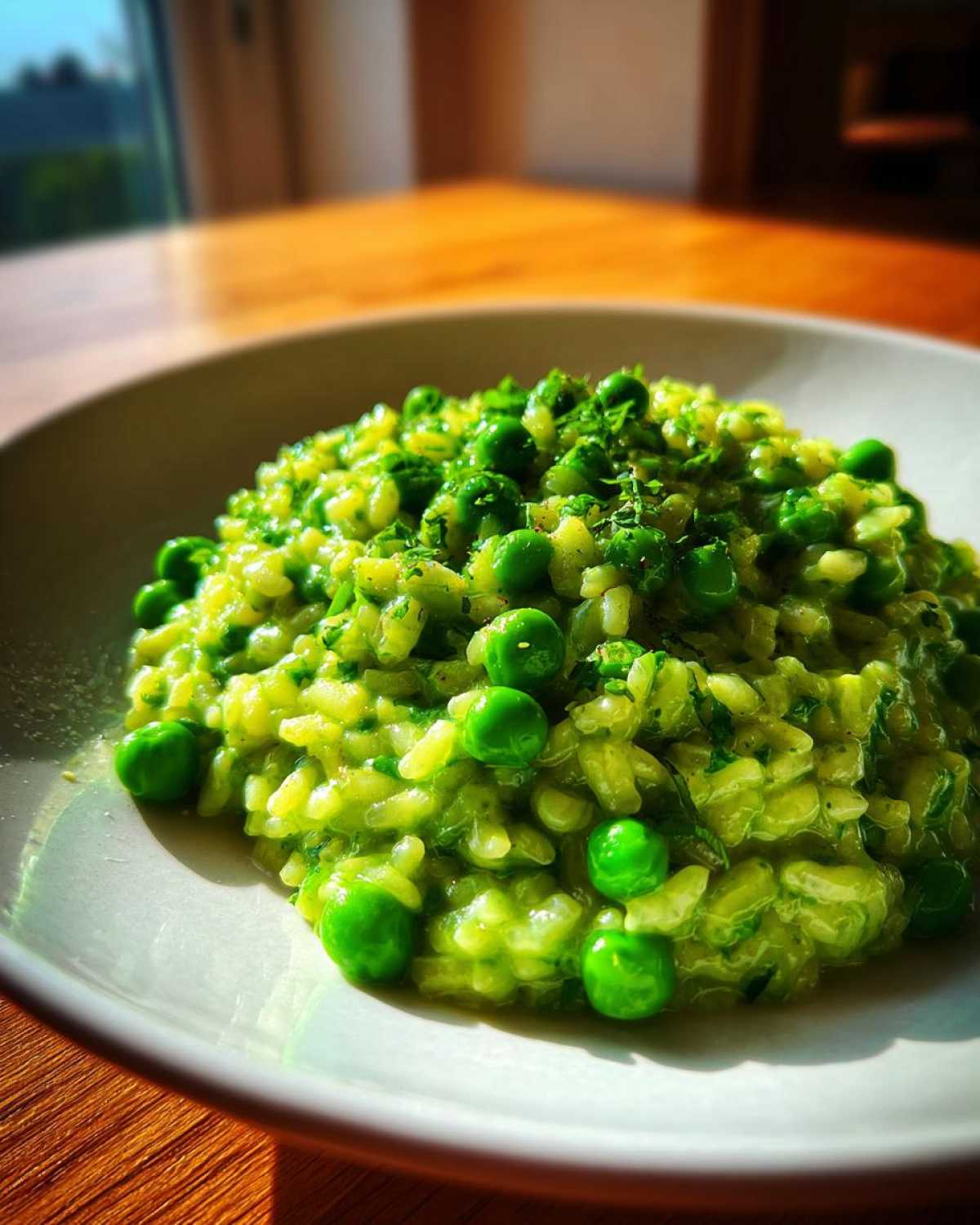 A close-up of creamy Spring Pea and Mint Risotto topped with whole peas and fresh herbs.