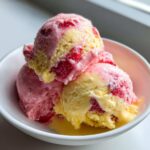 Three scoops of swirled strawberry banana ice cream, showing yellow banana and pink strawberry sections, served in a white bowl.