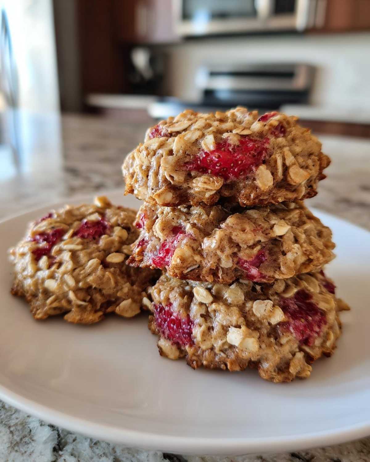 A stack of three delicious Strawberry Oatmeal Breakfast Cookies featuring visible oats and bright red strawberry pieces.